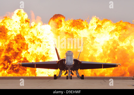 Un'F/A-18 Hornet siede sulla linea di volo come un muro di fuoco detona dietro di esso. Foto Stock