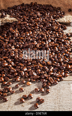 I chicchi di caffè su sfondo rustico - chicchi di caffè fuoriuscita da una tela o sacco di iuta su un listone rustico tavolo. Foto Stock