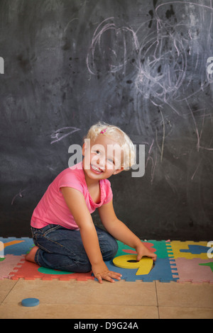 Sorridente ragazza che gioca con il numero puzzle di fronte a una lavagna Foto Stock