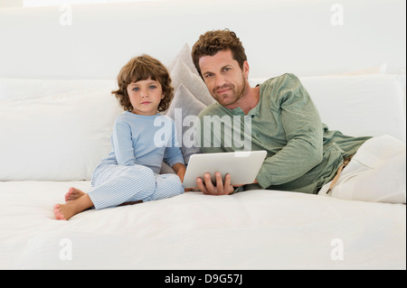 Uomo con una tavoletta digitale seduta sul letto con il suo figlio Foto Stock