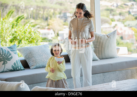 Ragazza con una ciotola di spuntini accanto alla madre azienda calici a stelo a casa Foto Stock