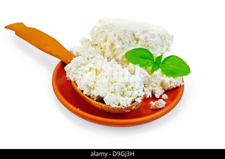 Il formaggio in un cucchiaio di legno e una lastra di argilla con un rametto di basilico verde isolato su sfondo bianco Foto Stock