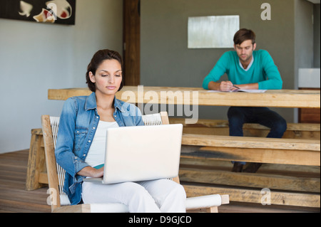 Donna che utilizza un computer portatile con il marito in background Foto Stock