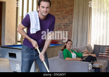 L'uomo tenendo un mop con sua moglie seduta su un divano Foto Stock
