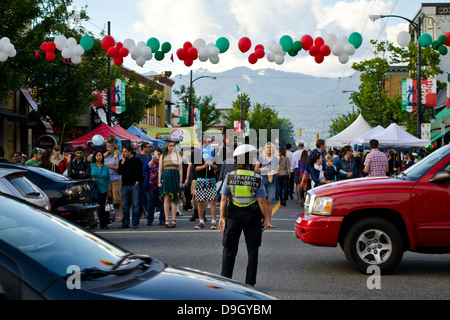 Un funzionario del traffico controlla il traffico intenso mentre la folla attende prima di attraversare la strada al giorno italiano street festival in East Vancouver. Foto Stock