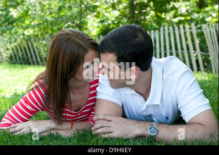 Giovane coppia caucasica giacente in erba guardando un altro amorevolmente Foto Stock