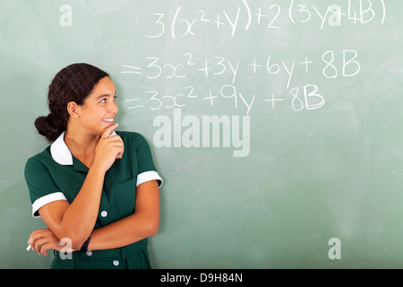 Femmina felice studente di scuola superiore in aula guardando la matematica scrivere sulla lavagna Foto Stock