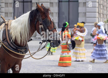 Un gruppo di giovani donne con fiori e indossando i tradizionali colorati abiti cubano stand beihnd un carro trainato da cavalli e attendono i turisti paganti per scattare la foto souvenir di essi sulla Plaza San Francisco nel centro della città di Havana, Cuba, 10 aprile 2013. Foto: Peter Zimmermann Foto Stock