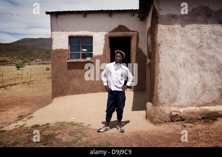 Giovane uomo recentemente restituita dalla città, si erge con orgoglio al di fuori della sua casa di famiglia in rural Transkei, Sud Africa Foto Stock