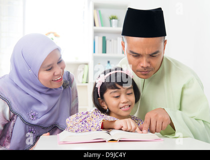 Malay musulmana di insegnamento dei genitori Bambino la lettura di un libro. Sud-est asiatico la famiglia a casa. Foto Stock