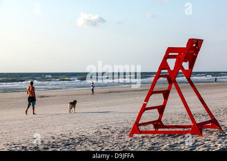 Iconico orange life guard sedia sulla Spiaggia di Jacksonville con un uomo a piedi un cane ed altri nuotare nell'Oceano Atlantico al di là. Foto Stock