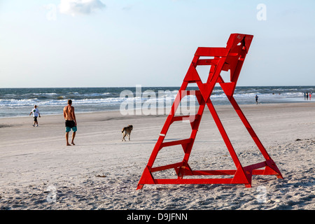 Iconico orange life guard sedia sulla Spiaggia di Jacksonville con un uomo a piedi un cane ed altri nuotare nell'Oceano Atlantico al di là. Foto Stock