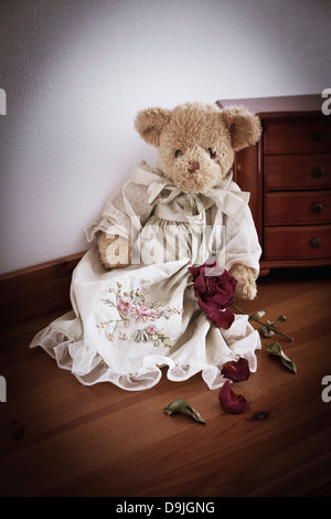 Triste guardando orsacchiotto con secchi Red Rose fiore seduto su un tavolino. Foto Stock