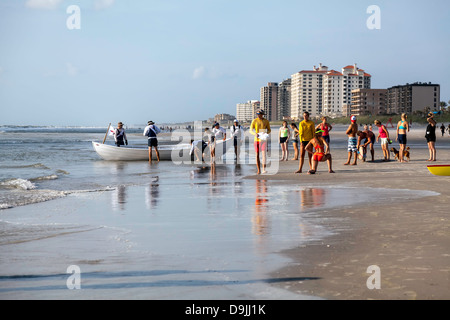 Gli uomini e le donne in competizione in quarto Annual JAX Beach Paddling Challenge con surf barca di salvataggio e i volontari in background. Foto Stock