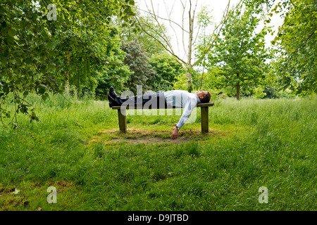 Un imprenditore si trova in posizione supina su un banco di legno in Regent's Park di Londra. Paesaggio. Foto Stock