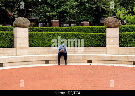 Uomo con una pastiglia seduto fuori della British Library di Londra. Egli siede tra due Antony Gormley sculture su plinti. Foto Stock