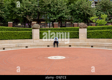 Uomo con una pastiglia seduto fuori della British Library di Londra. Egli siede tra due Antony Gormley sculture su plinti. Foto Stock