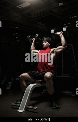 Muscolare di giovane uomo di eseguire la spalla si solleva con manubri in palestra Foto Stock