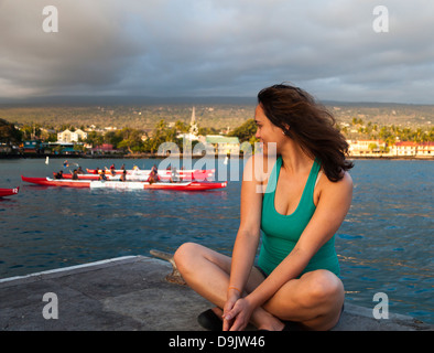 Donna seduta sul molo di Kailua-Kona sulla Big Island delle Hawaii guardando canoe outrigger Foto Stock