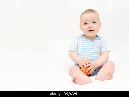 Bella happy baby boy seduta sul letto bianco con Apple Foto Stock