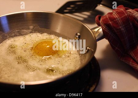 Uovo cotto pollo mangiare cibo pasto bianchi tuorlo delle uova commestibili di colesterolo in padella cuocere la spatola stufa asciugamano rosso maniglia sale pepe Foto Stock