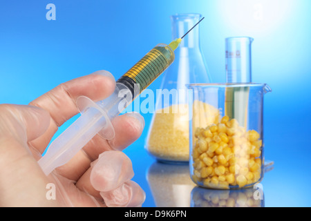 Mano con la siringa e la tazza di misura con il mais Foto Stock