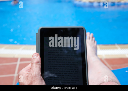 L'uomo la lettura di ebook su tablet PC dal lato di una piscina in vacanza Salou Costa Dorada Spagna Foto Stock