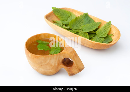 Melissa (Melissa officinalis) tè alle erbe in un Kuksa al fianco di una ciotola di legno contenente le foglie Foto Stock
