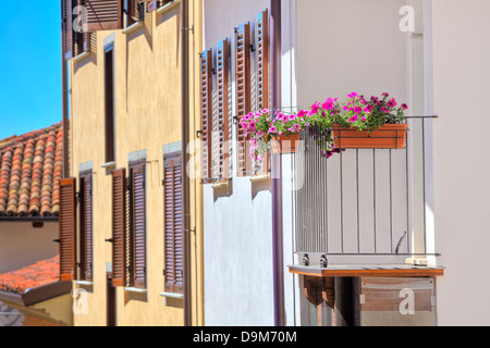 Fiori in vaso sul balcone di una tipica casa italiana con persiane di legno e un tetto di tegole nella città di La Morra in Italia. Foto Stock