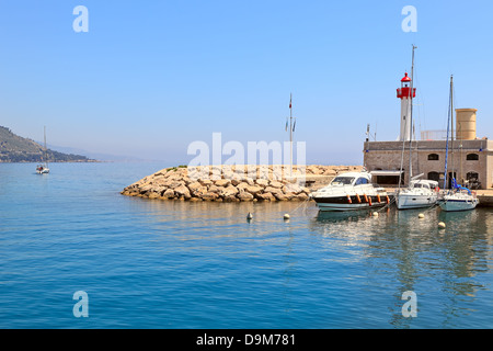 Yachts, barca e piccolo faro all'entrata a marina di Menton - cittadina sulla riviera francese. Foto Stock