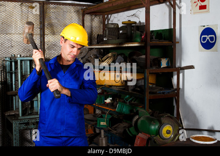 In fabbrica il collare blu lavoratore con grande martello in officina Foto Stock