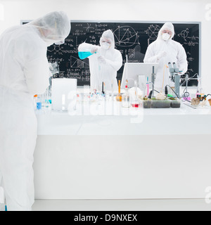 General-vista di tre scienziati in un laboratorio di chimica di condurre un esperimento intorno ad una tabella lab con liquidi colorati e laboratorio per Foto Stock