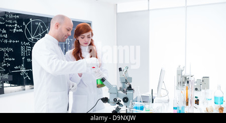 Vista laterale di un insegnante conducendo un esperimento di laboratorio con uno studente intorno alla tabella lab con strumenti di laboratorio, liquidi colorati e un bl Foto Stock