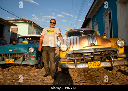 Orgoglioso uomo cubano con il suo classico siamo auto su una strada di ciottoli nella città vecchia di Trinidad, Cuba, Caraibi Foto Stock