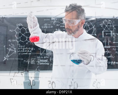 Close-up di scienziato conduce un laboratorio di chimica esperimento con liquidi colorati e una lavagna con le formule sulla ba Foto Stock