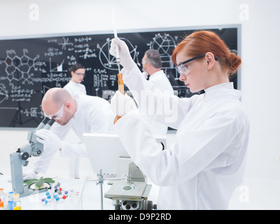 Close-up di uno studente nel laboratorio di chimica di condurre un esperimento con iquids colorati e un altro tre persone analizzando i dati Foto Stock