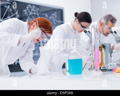 Close-up di tre persone in un laboratorio di chimica conduzione di esperimenti di chimica su una tabella lab con strumenti di laboratorio e liquidi colorati Foto Stock