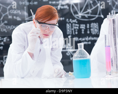 Close-up di studente in un laboratorio di chimica di condurre un esperimento con colorati di liquidi e di gas in una tabella lab con una lavagna o Foto Stock