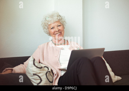 Felice senior donna seduta sul divano di casa con il computer portatile Foto Stock