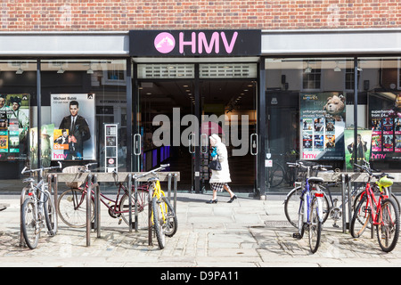 Signora anziana passeggiate passato un HMV shop a Chichester, con biciclette parcheggiate fuori. Foto Stock