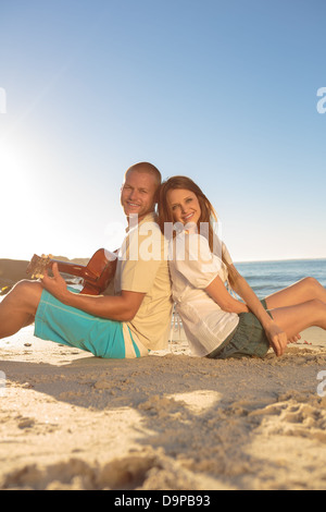 Coppia giovane sat back-to-back sulla spiaggia Foto Stock