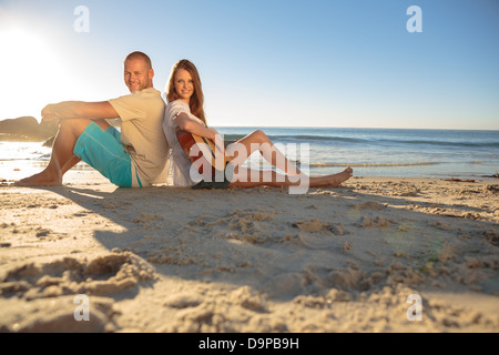 Coppia felice sat back-to-back sulla spiaggia Foto Stock