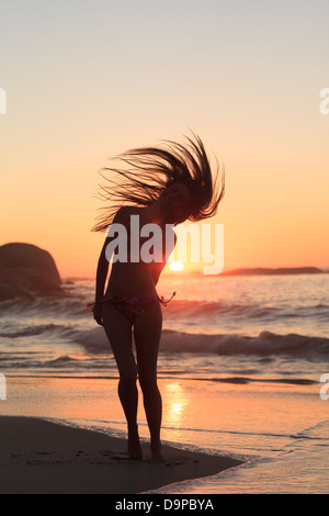 Donna in piedi sulla spiaggia nel lanciare i suoi capelli Foto Stock