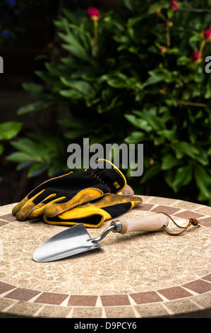 Cazzuola a mano con i guanti su un tavolo da giardino. Foto Stock