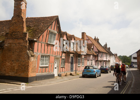 Lavenham Suffolk East Anglia England Due ciclisti pedalando attraverso il terrazzo di color pastello metà case con travi di legno borgo medievale Foto Stock