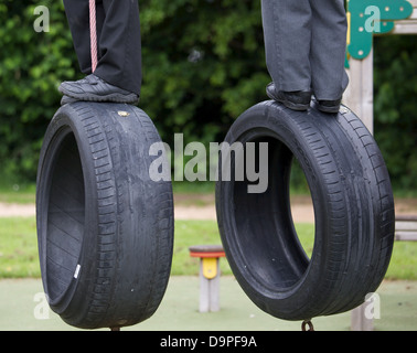 Due scolari equilibrio sui due pneumatici penzolante in un parco giochi a scuola Foto Stock