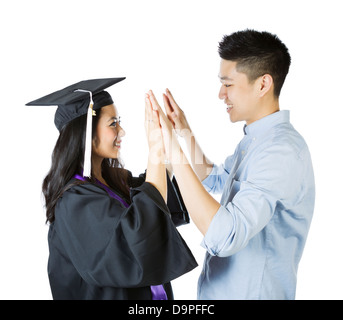 Foto di giovane donna adulta, vestito in abito di graduazione e cappuccio, ricevere complimenti, con un high five, dal suo fidanzato sul Foto Stock