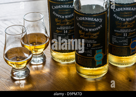 Tre bottiglie di botte forza single malt whisky con due metà piena bicchieri su una tavola di legno Foto Stock