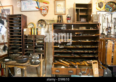 Vintage ghisa pentole, padelle e attrezzi memorizzati nelle tabelle e nei cassetti e scaffalature in legno. Le immagini e gli strumenti appendere alla parete. Foto Stock