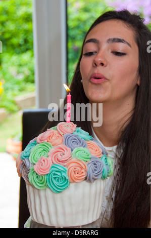 Chiudere verticale su ritratto di una ragazza di compleanno soffiando fuori la candela sul suo torte fatte in casa Foto Stock